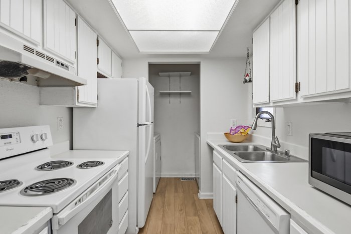 A galley kitchen with white cabinets and a skylight edited by AutoHDR V3