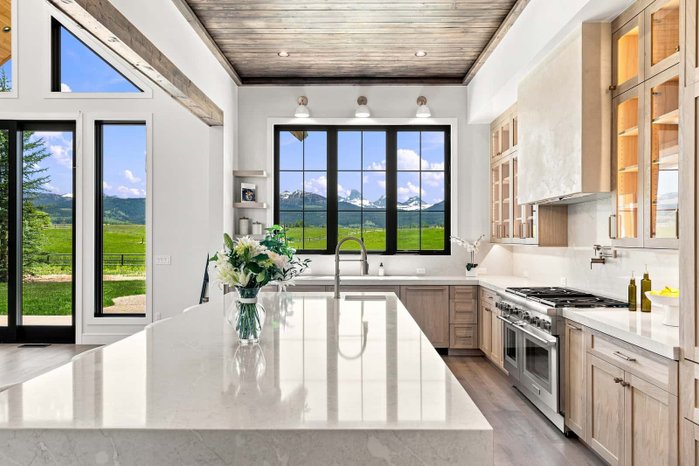 A kitchen island beneath mountain-view windows edited by AutoHDR Iris